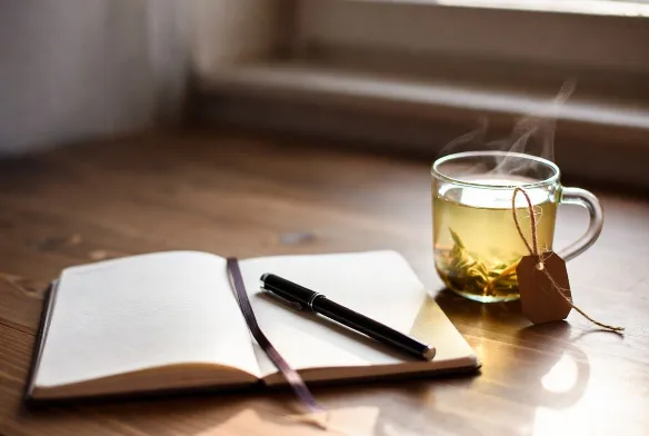 Açık bir defter, kalem ve bir fincan bitki çayı