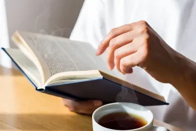 Telefonu bir kenara bırakıp kitap ve çayla vakit geçiren kişi